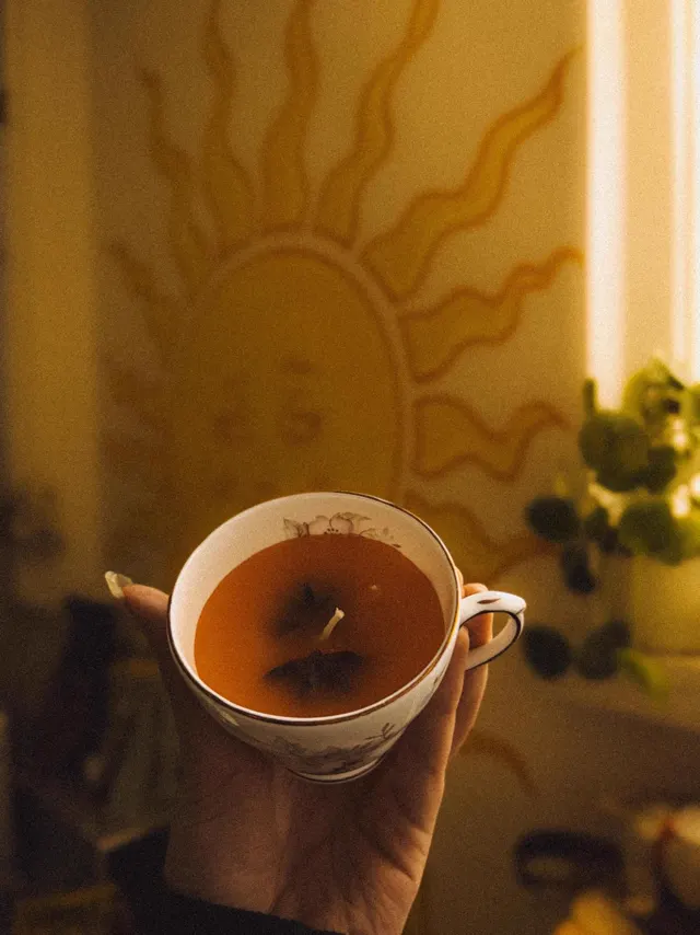 A teacup candle held up against a painted sun